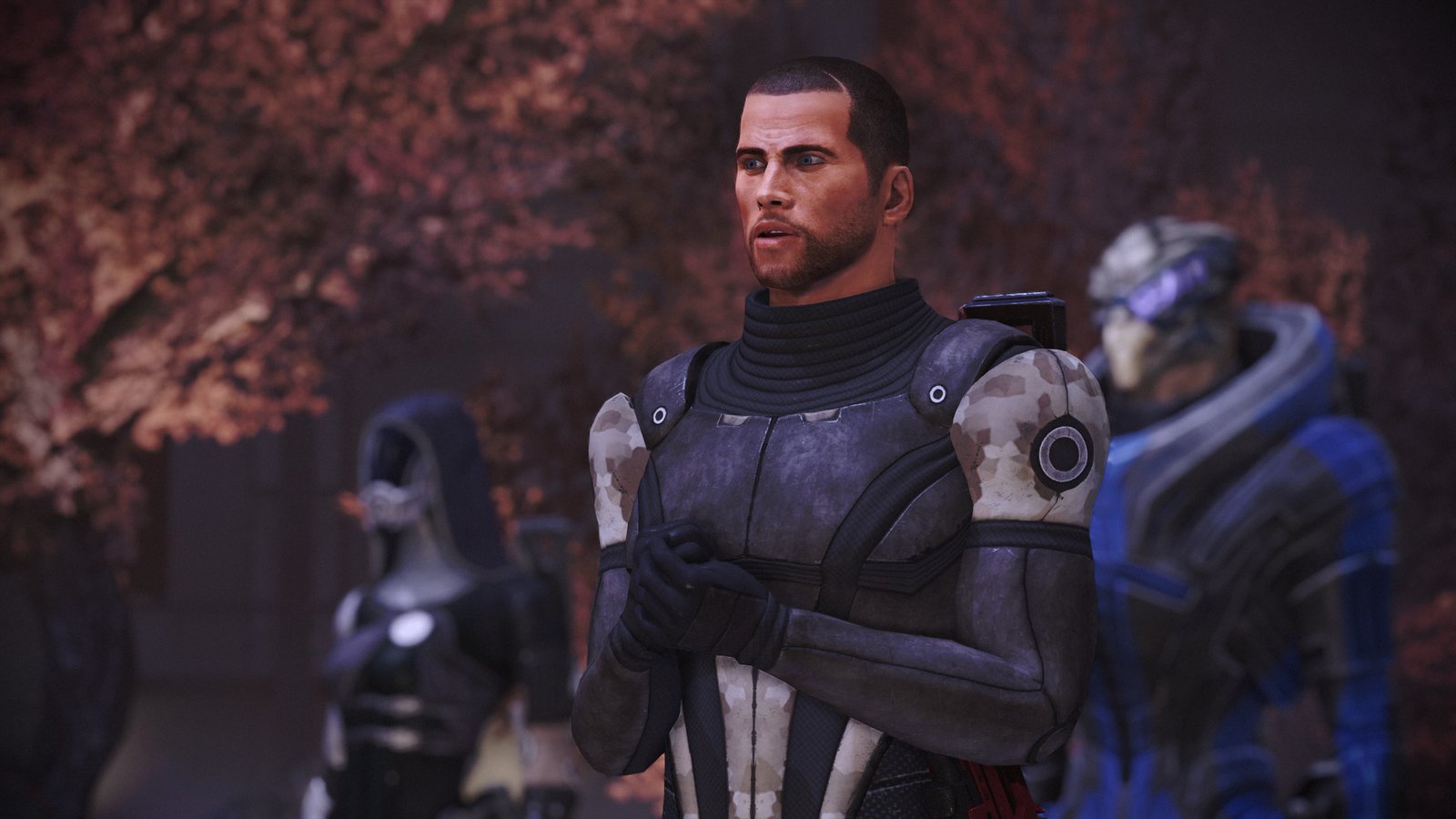 Man with short hair and in military armour in the foreground. A woman in a suit covering her entire body and face, and an alien looking male humanoid, stand in the background.