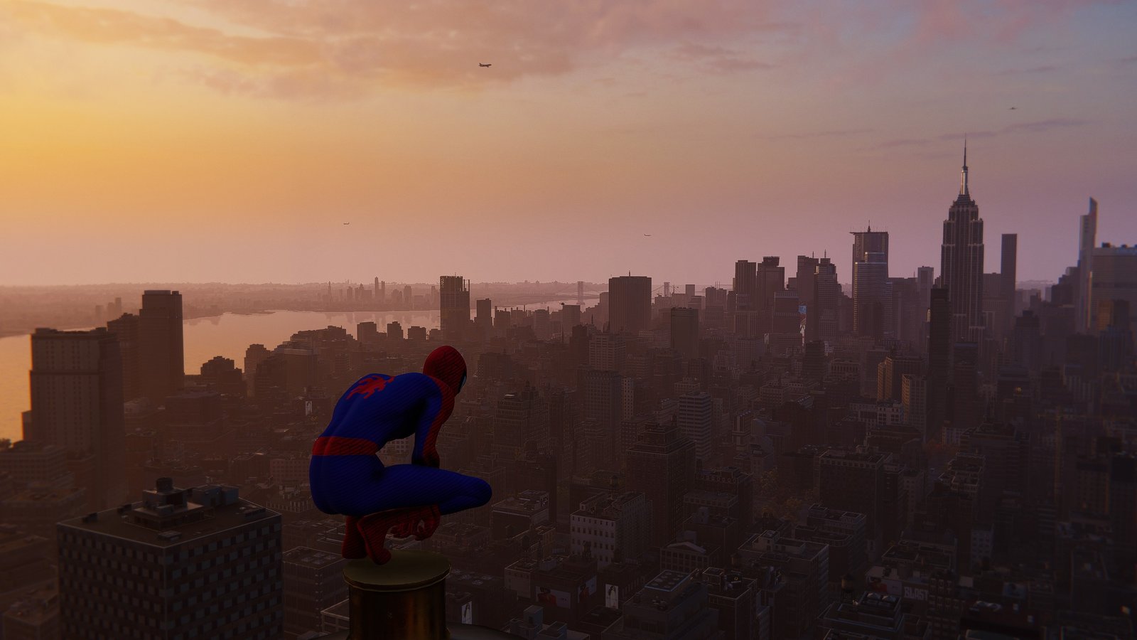 Spiderman sits at the very top of a skyscraper, overlooking New York City as the sun sets.